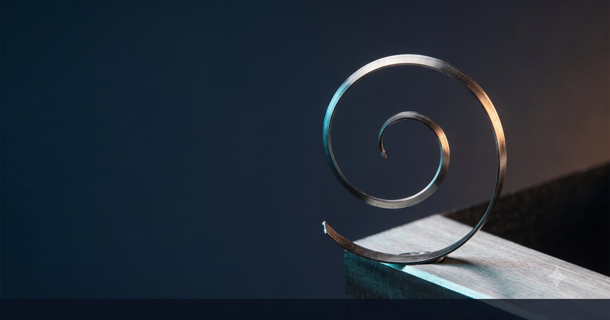A curl of steel shaving lifting off a freshly machined surface, cyan light raking one edge and amber catching the other